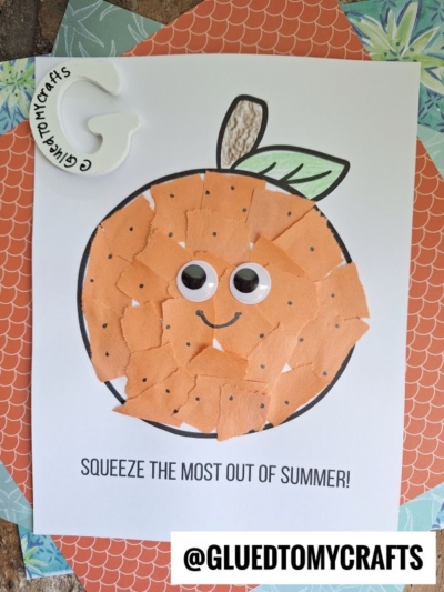 A handmade torn paper orange craft with googly eyes and a smile sits on a white sheet, featuring "Squeeze the most out of summer!" text. The username @GLUEDTOMYCRAFTS is at the bottom.