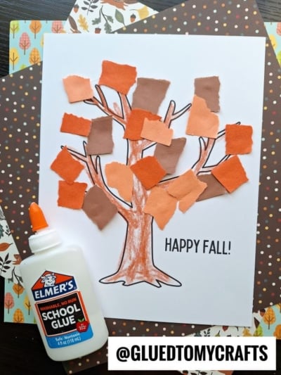 A fall craft project featuring a hand-drawn torn paper tree with orange and brown paper leaves, a bottle of glue, patterned papers, and the text HAPPY FALL! and @GLUEDTOMYCRAFTS on the image.