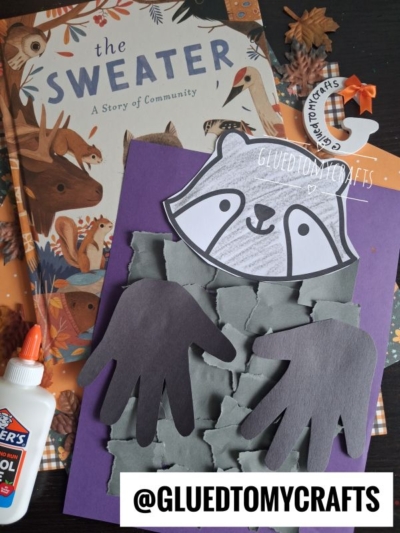 Childrens torn paper raccoon craft made with gray paper squares and hand cutouts, a purple background, glue, and the book The Sweater with woodland animals. Instagram handle @GLUEDTOMYCRAFTS.