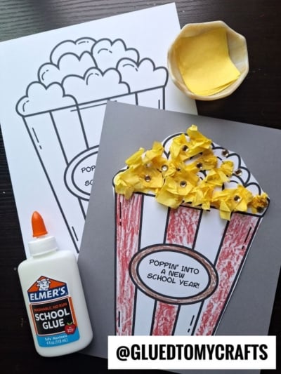 A school-themed craft featuring a back to school popcorn coloring page, a finished version with yellow tissue paper as popcorn, a glue bottle, and a bowl of yellow tissue paper pieces. Text: @GLUEDTOMYCRAFTS.