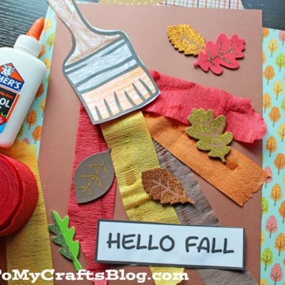 A fall paint brush craft featuring a paper paintbrush, colored crepe paper strips, glittery leaf cutouts, and “HELLO FALL” on brown paper.