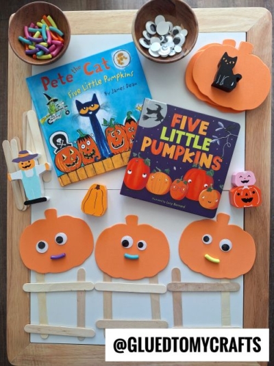 A flat lay of Halloween crafts, perfect for FALL THEMED SENSORY BIN IDEAS, with paper pumpkins, popsicle stick fences, a black cat, pumpkin erasers, googly eyes, felt-tip markers, and two children's books: Pete the Cat: Five Little Pumpkins and Five Little Pumpkins.