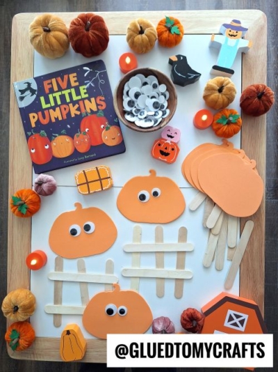A tray displays the book “Five Little Pumpkins,” orange foam pumpkin shapes, googly eyes, craft sticks, felt pumpkins, a scarecrow sticker, and other pumpkin crafts—perfect inspiration for FALL THEMED SENSORY BIN IDEAS.