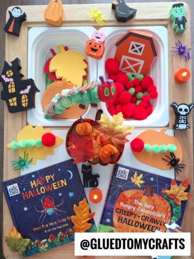 A Halloween-themed sensory tray featuring felt pumpkins, foam shapes, pom-poms, autumn leaves, Halloween books, and toy caterpillars—perfect for exploring FALL THEMED SENSORY BIN IDEAS. @GLUEDTOMYCRAFTS text at the bottom.