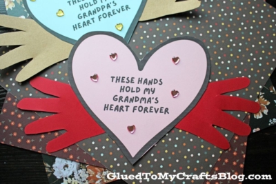Two heart-shaped cards, one blue and one pink, each decorated with gold heart stickers and handprints. Perfect for Grandparent's Day, each card says, These hands hold my heart forever—one for Grandpa and one for Grandma.