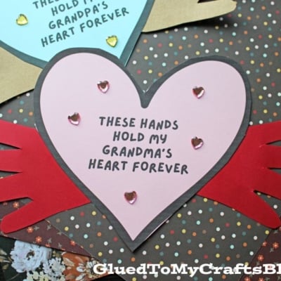 Two heart-shaped cards, one blue and one pink, each decorated with gold heart stickers and handprints. Perfect for Grandparent's Day, each card says, These hands hold my heart forever—one for Grandpa and one for Grandma.