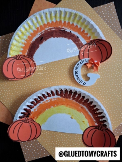 Two Paper Plate Fall Rainbow crafts painted in vibrant autumn hues, each adorned with paper pumpkins and set against an orange polka dot background. Craft tags read @GLUEDTOMYCRAFTS.