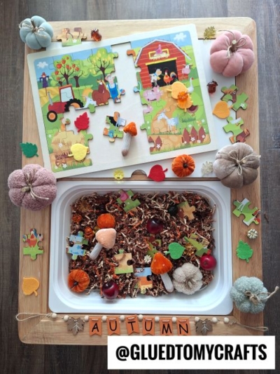 Explore our FALL THEMED SENSORY BIN IDEAS with this sensory tray featuring autumn items, a farm puzzle, faux pumpkins, mushrooms, acorns, apples, and wooden leaves—perfectly arranged around a bin labeled AUTUMN and @GLUEDTOMYCRAFTS.