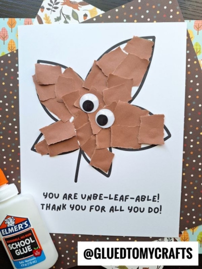 A torn paper leaf craft with brown paper pieces and two googly eyes on a leaf outline. Text reads You are unbe-leaf-able! Thank you for all you do! Elmers glue and polka dot paper are nearby.