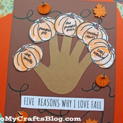 A fall craft featuring a paper handprint with five reasons to love fall, each on a pumpkin cutout, surrounded by mini pumpkins and leaves. Text reads Five Reasons Why I Love Fall!