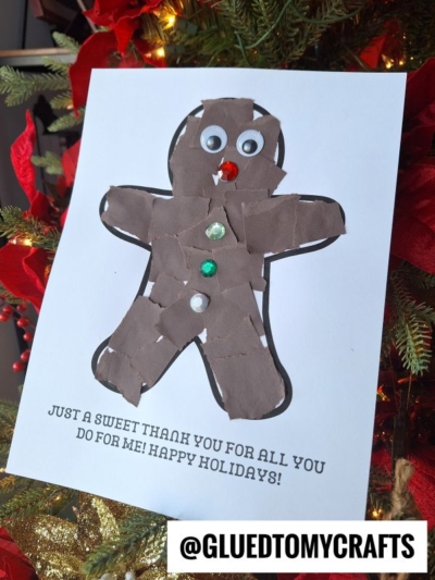 Handmade holiday thank-you card featuring a torn-paper gingerbread man with googly eyes, a red gem nose, and colorful gem buttons, displayed in front of a decorated Christmas tree, with the message: “Just a sweet thank you for all you do for me! Happy Holidays!”