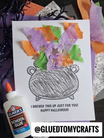 A Halloween craft features a torn paper witch cauldron with colorful crepe paper and star shapes as potion, a bottle of glue, and spiderweb-patterned paper in the background. Text says I brewed this up just for you! Happy Halloween!.