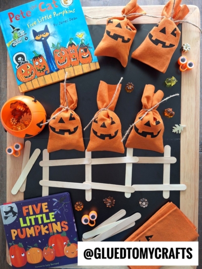 A Halloween craft setup featuring pumpkin treat bags, Pete the Cat: Five Little Pumpkins and Five Little Pumpkins books, craft sticks arranged as a fence, black and orange confetti, small pumpkin decorations, and fall themed sensory bin ideas.