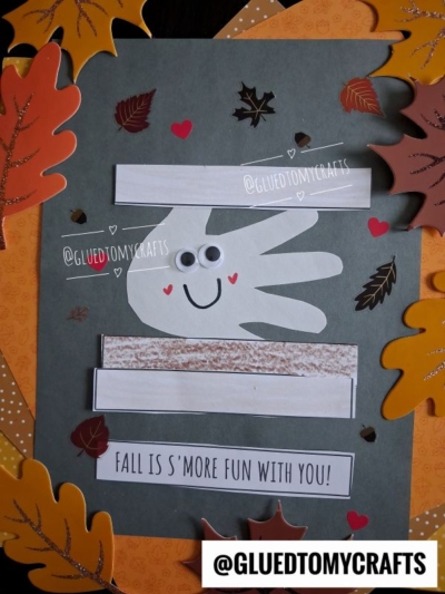 A fall-themed craft features a handprint smores keepsake with googly eyes and a smile, surrounded by colorful paper leaves and the text FALL IS SMORE FUN WITH YOU! and @GLUEDTOMYCRAFTS.