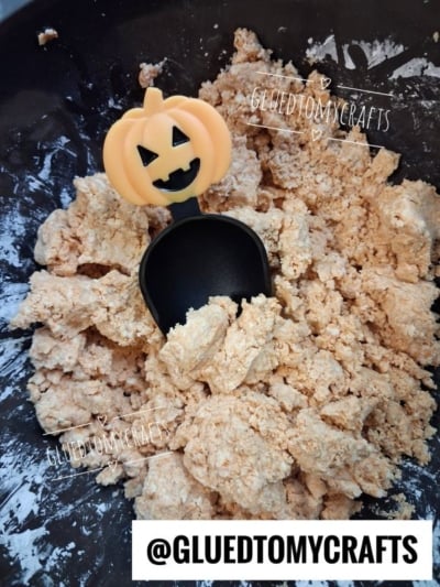 A mixing bowl of crumbly Pumpkin Spice Cloud Dough with a black scoop featuring a smiling jack-o-lantern handle. The watermark @GLUETOMYCRAFTS appears multiple times on the image.