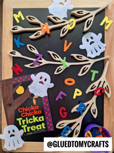 A Halloween-themed alphabet activity inspired by FALL THEMED SENSORY BIN IDEAS features felt letters, wooden branches, ghost shapes, and the book Chicka Chicka Tricka Treat on a chalkboard, with @GLUEDTOMYCRAFTS displayed.