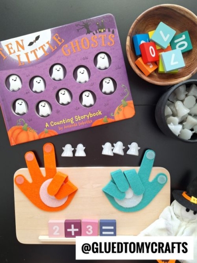 A counting book titled Ten Little Ghosts, ghost-shaped counters, colorful number and math symbol blocks, felt hand shapes, and a math board arranged on a table offer fun fall themed sensory bin ideas for a Halloween math activity.