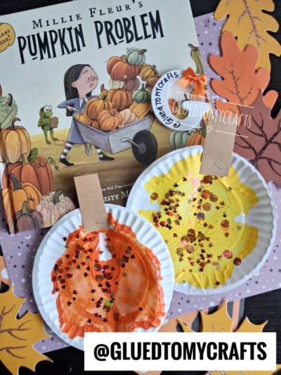 Childrens book Pumpkin Problem with two orange paper plate pumpkin crafts, including a fun paint splat pumpkin design, decorated with glitter, clipped with clothespins, and surrounded by fall leaf cutouts. @GLUEDTOMYCRAFTS appears at the bottom.