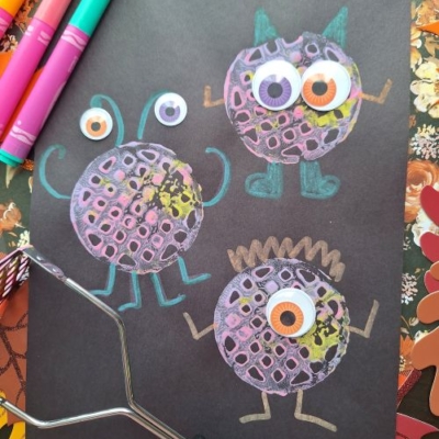 Three colorful, round monsters with googly eyes, drawn on black paper using chalk and paint. Markers and a potato masher hint at this fun potato masher stamped craft. The @GLUEDTOMYCRAFTS handle appears at the bottom.