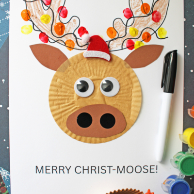 A cupcake liner moose head design, in the center of white cardstock paper, covered with Christmas lights made from a child's thumb dipped in craft paint