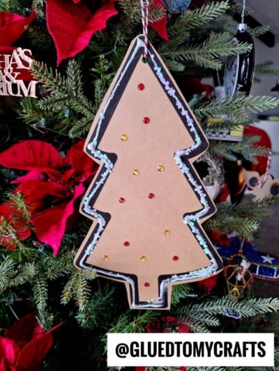 Cardboard Christmas tree ornament with small red and yellow dots hangs on a decorated tree with red poinsettias and green branches, making it a charming addition to any Paper Gingerbread Tree Craft display. @GLUEDTOMYCRAFTS text is at the bottom.