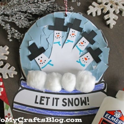 A handmade torn paper snow globe craft features blue and white paper, snowmen faces, cotton ball snow, and "LET IT SNOW!" at the base. Elmer’s glue and snowflake decorations complete this fun winter project.