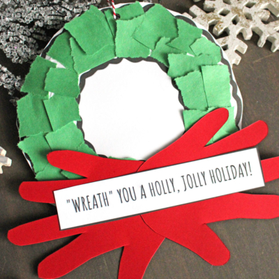 A handmade torn paper Christmas wreath craft made from green paper pieces, a red bow, and a white center with a note reading “‘Wreath’ you a holly, jolly holiday!” Snowflakes and a “Free Printable!!!” label are also visible.