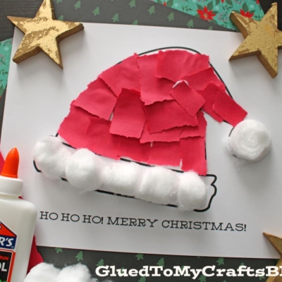 A Christmas craft featuring a torn paper Santa hat made from red paper and cotton balls on a printable with HO HO HO! MERRY CHRISTMAS! text