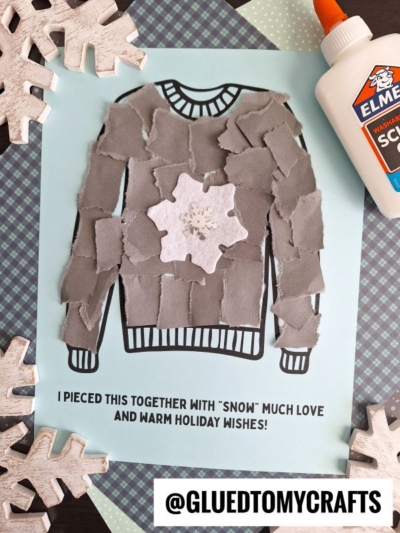 A craft project displays a torn paper winter sweater adorned with gray pieces and a white snowflake, surrounded by snowflake cutouts, a glue bottle, and layered paper. Text: “I pieced this together with ‘snow’ much love and warm holiday wishes!”.