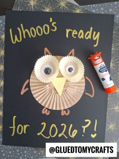 A handmade owl crafted from cupcake liners and googly eyes is glued to black paper with “Whooo’s ready for 2026?!”—a fun idea for New Year’s Eve Crafts For Kids. A glue stick and the handle @GLUEDTOMYCRAFTS appear in the image.
