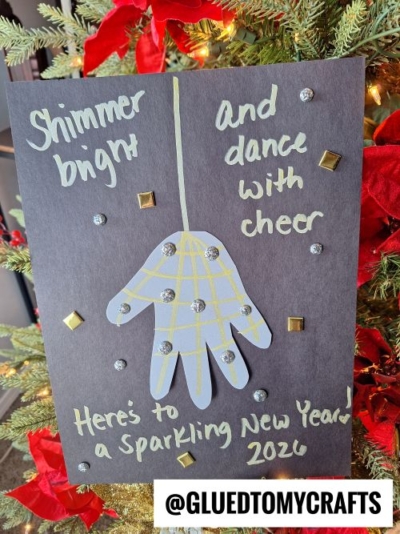 A handmade New Year’s card with a handprint ornament design, silver gems, and gold square decorations—perfect for New Year’s Eve Crafts For Kids. The card reads: Shimmer bright and dance with cheer. Here’s to a Sparkling New Year! 2026.
