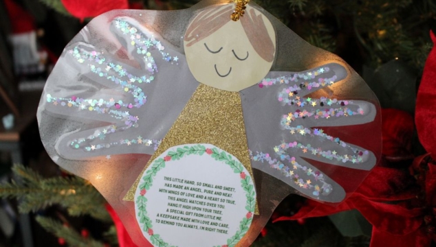 A handmade handprint angel ornament with glittery wings and a heartfelt poem, hanging on a Christmas tree.