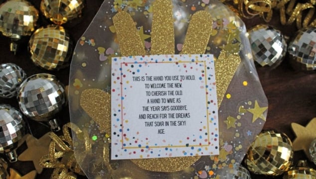 A new year's eve handprint craft with gold glitter and confetti surrounds a poem about saying goodbye to the old year. Disco ball ornaments and gold ribbon decorate the background.