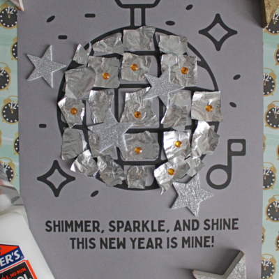 A handmade New Year’s craft features a torn paper disco ball made from foil squares and silver glitter stars on gray paper. Text reads, “Shimmer, sparkle, and shine. This New Year is mine!” A glue bottle and “Free Printable!” are also visible.