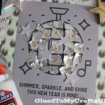 A handmade New Year’s craft features a torn paper disco ball made from foil squares and silver glitter stars on gray paper. Text reads, “Shimmer, sparkle, and shine. This New Year is mine!”