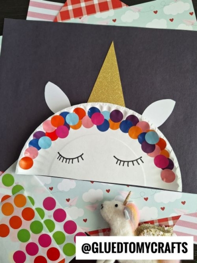 A unicorn craft made from a paper plate decorated with colorful circle stickers as a mane, a gold paper horn, closed eyes drawn on, and pastel papers in the background—perfect for kids who love coding label crafts and unicorns alike.