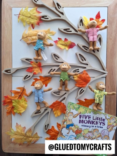 Five monkey dolls in colorful clothes sit on a decorative tree with artificial autumn leaves, perfect for inspiring FALL THEMED SENSORY BIN IDEAS. The book Five Little Monkeys Sitting in a Tree and a @GLUEDTOMYCRAFTS label are at the bottom right.