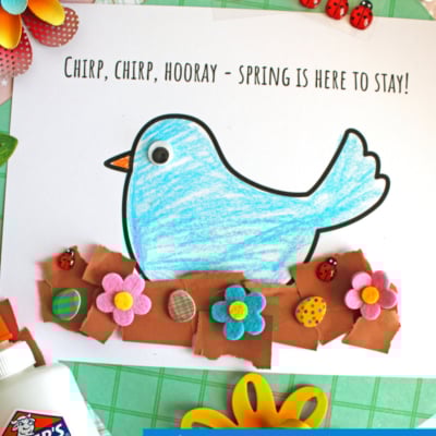 A colorful spring craft features a blue paper bird on a white sheet with Chirp, chirp, hooray – spring is here to stay! Brown torn paper forms a nest, decorated with paper flowers. Elmer’s glue and buttons are nearby.
