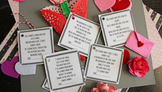 A flat lay of handmade Valentine’s Day cards and decorations, including paper flowers, felt hearts, an envelope, and printed cards with romantic poems, arranged on a gray and pink background.