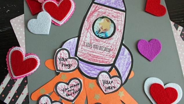 A handmade card with a rocket drawing, hearts, and messages of love. Felt hearts and an envelope are around it.