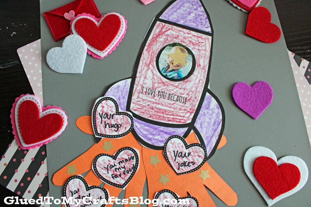 A handmade card with a rocket drawing, hearts, and messages of love. Felt hearts and an envelope are around it.