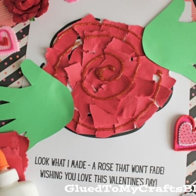 A handmade Valentine’s Day craft featuring a red rose made of torn paper, two green handprint leaves, a glue bottle, heart decorations, and a message: “LOOK WHAT I MADE - A ROSE THAT WON’T FADE! WISHING YOU LOVE THIS VALENTINE’S DAY!”.