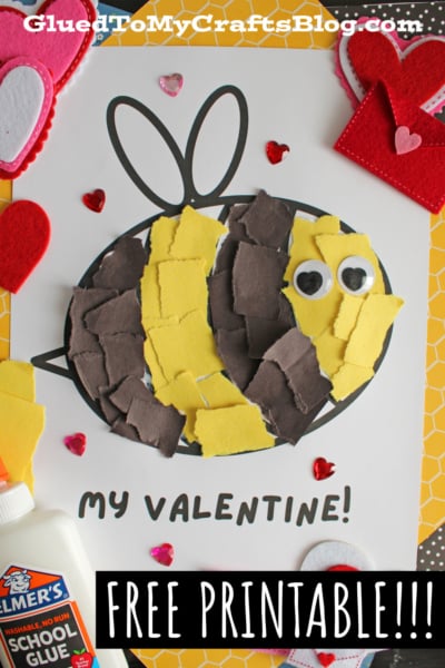 A cheerful Valentine's Day craft featuring a bumblebee made from torn yellow and black paper on a white sheet with "MY VALENTINE!" written below. The bee has googly eyes with heart-shaped pupils and is surrounded by felt hearts, heart-shaped gems, and patterned papers. A bottle of Elmer's School Glue is visible in the corner, emphasizing the hands-on crafting process.