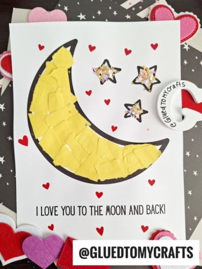 A handmade card features a yellow, torn paper moon, three decorated stars, and red hearts on white paper. Text below reads, I LOVE YOU TO THE MOON AND BACK! with @GLUEDTOMYCRAFTS displayed at the bottom.