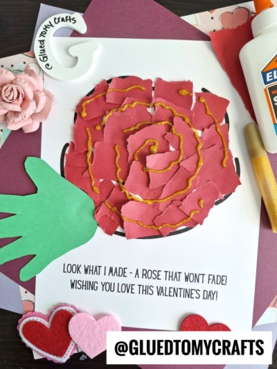 A handmade Valentine’s Day torn paper rose card featuring a rose made from torn red paper and gold glitter glue, with a green handprint cutout for the leaf, pink and red heart felt decorations, a paper flower, and glue.