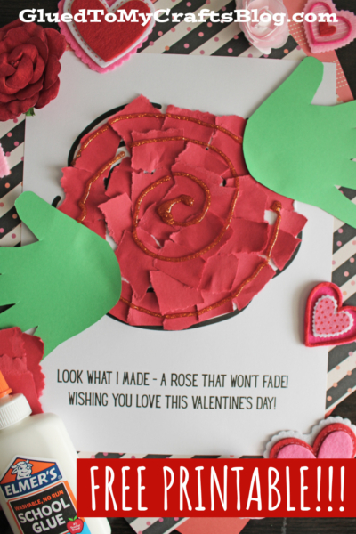 A handmade rose Valentine’s Day craft made from red paper pieces with glitter on a printed sheet that reads, A rose that wont fade! Green paper leaves, Elmer’s glue bottle, and heart decorations surround the craft.