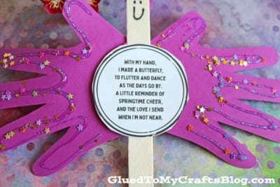 A purple paper butterfly made from handprint cutouts is decorated with glitter and a smiling face. A round poem about sending love is in the center. The background is colorful and the GluedToMyCraftsBlog.com watermark is visible.