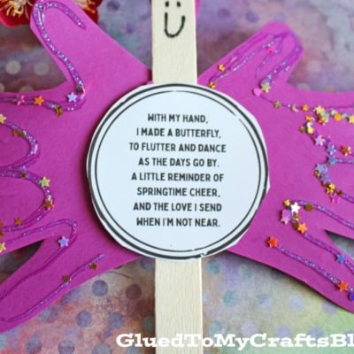 A purple paper butterfly made from handprint cutouts is decorated with glitter and a smiling face. A round poem about sending love is in the center. The background is colorful and the GluedToMyCraftsBlog.com watermark is visible.