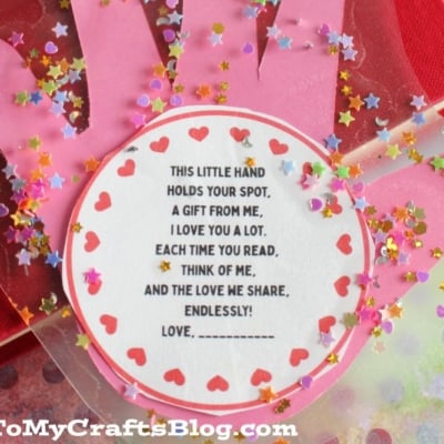 A pink hand-shaped bookmark with red heart stickers and star confetti surrounds a round note that reads a heartfelt message about love and reading. The image is from GluedToMyCraftsBlog.com.