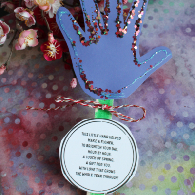 A purple handprint craft with glitter edges is attached to a green stick, with a round tag featuring a poem. Flowers and colorful backgrounds surround it. Text reads GluedToMyCraftsBlog.com and FREE PRINTABLE!!!.